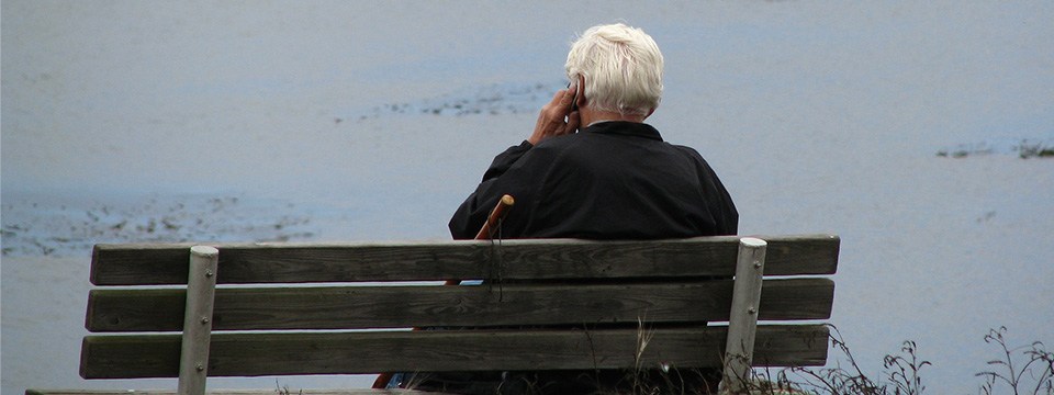 elderly man sitting on a bench on his phone